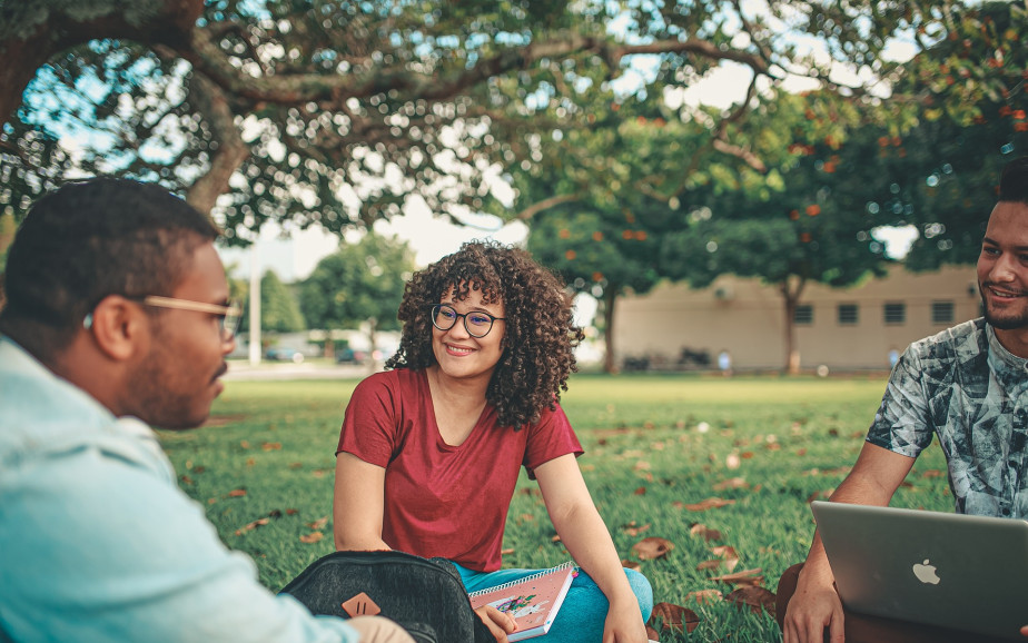 Three international tertiary students sit on the grass under a tree