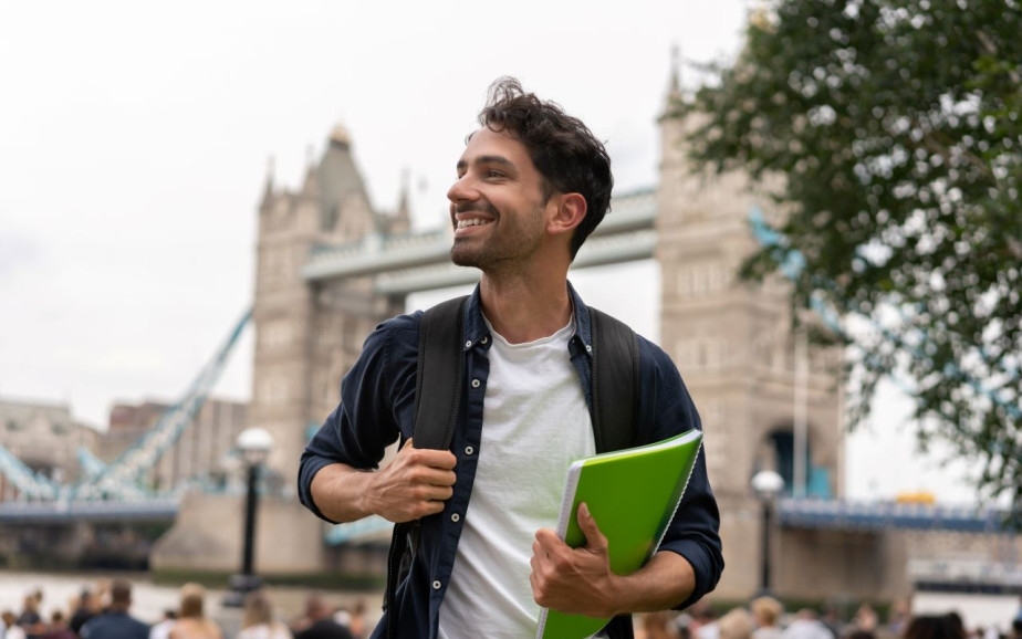 A young man stands in London holding a file.