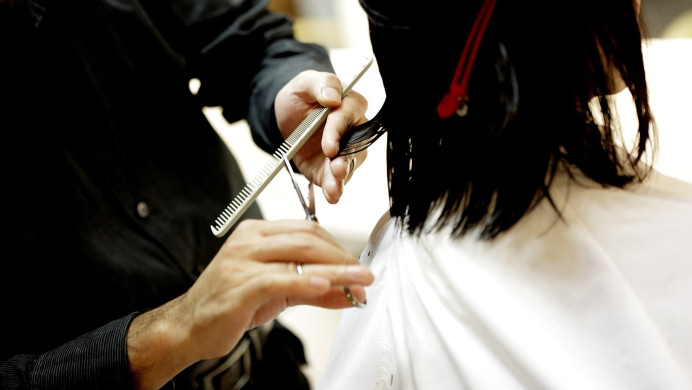 A trainee hairdresser cuts a client's hair