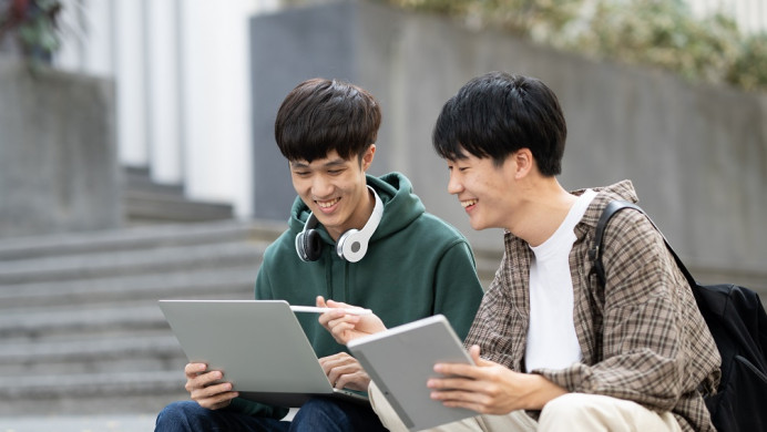 Two students sit on stairs looking at laptop